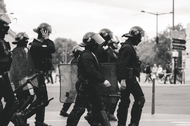 black and white photo featuring SWAT team walking in uniform with shield